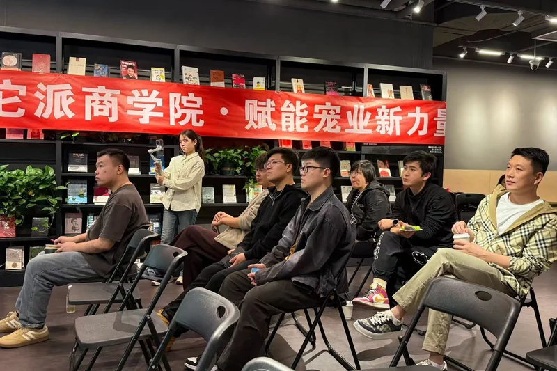 参与者坐在室内参加交流活动，背后有洗它派商学院横幅